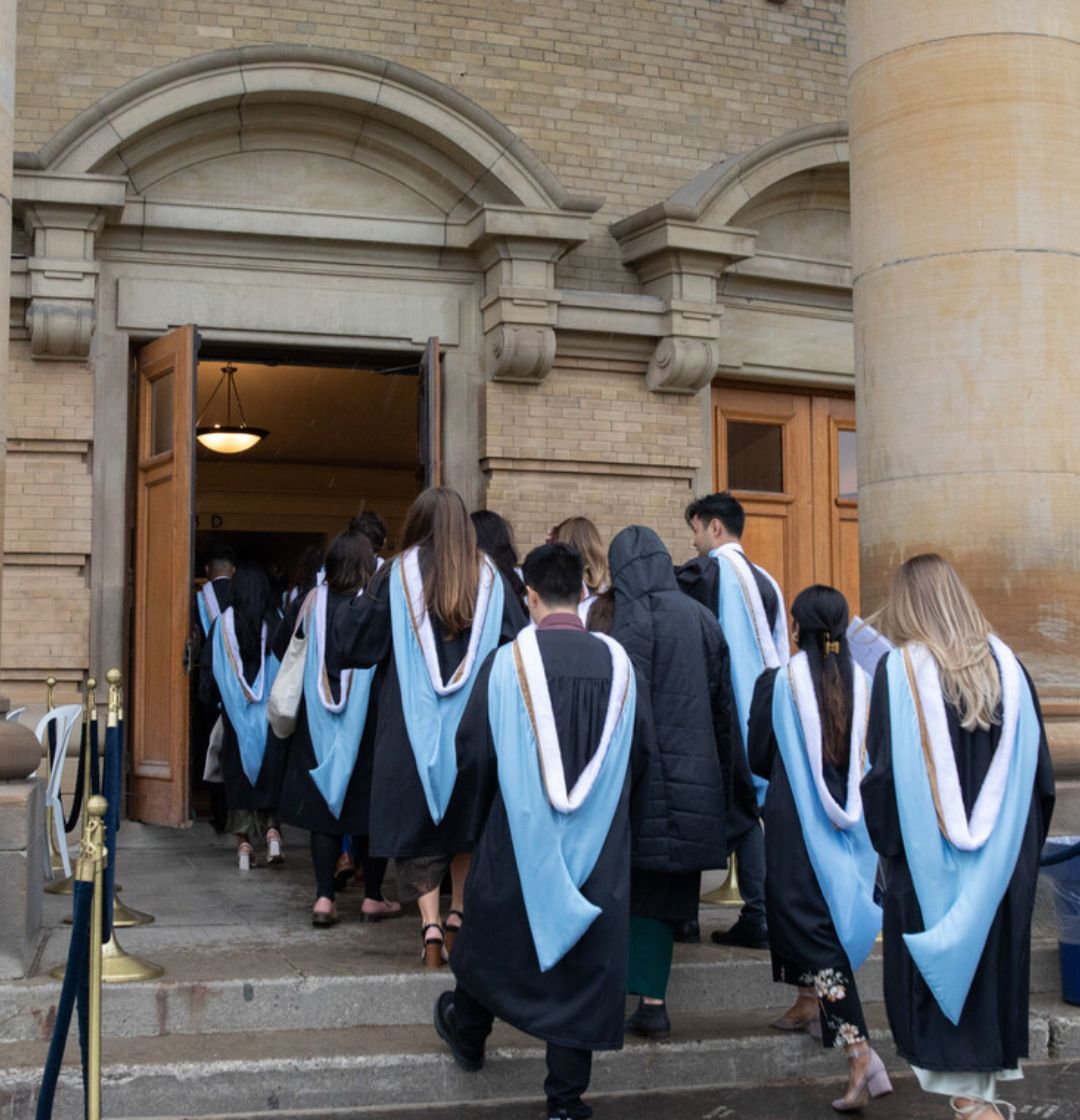 students in convocation robes walking into convocation hall